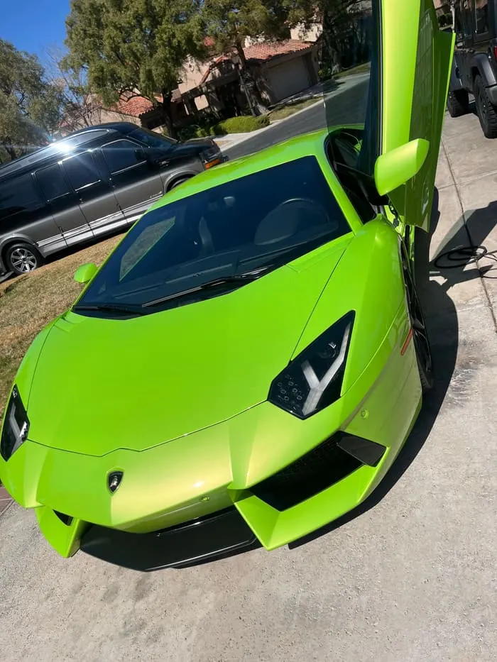 Green Lamborghini Aventador front three-quarter with scissor door raised after detailing
