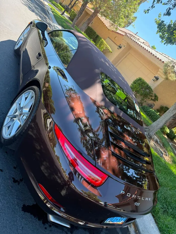 Porsche 911 Cabriolet rear three-quarter with corrected paint mirroring the treeline